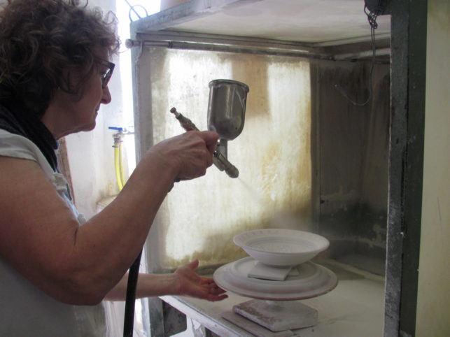 la ceramista Laura Silvagni spruzza la cristallina prima di infornare le ceramiche